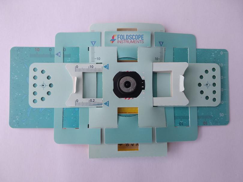 A photograph of a Foldscope, which is a microscope made from folded paper and light lenses.
